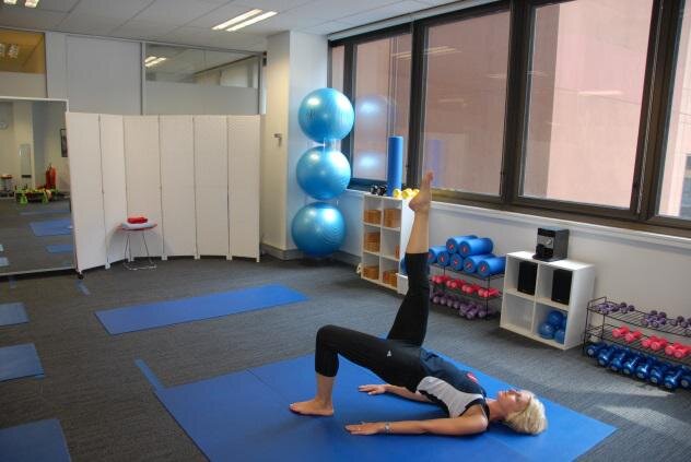 The HealthFit studio: a bright room with blue mats and exercise balls, Christine demonstrating on the floor.