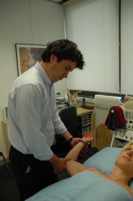 Darren Jenkins assessing a patient's arm in the consulting room at Collins Street Physiotherapy.