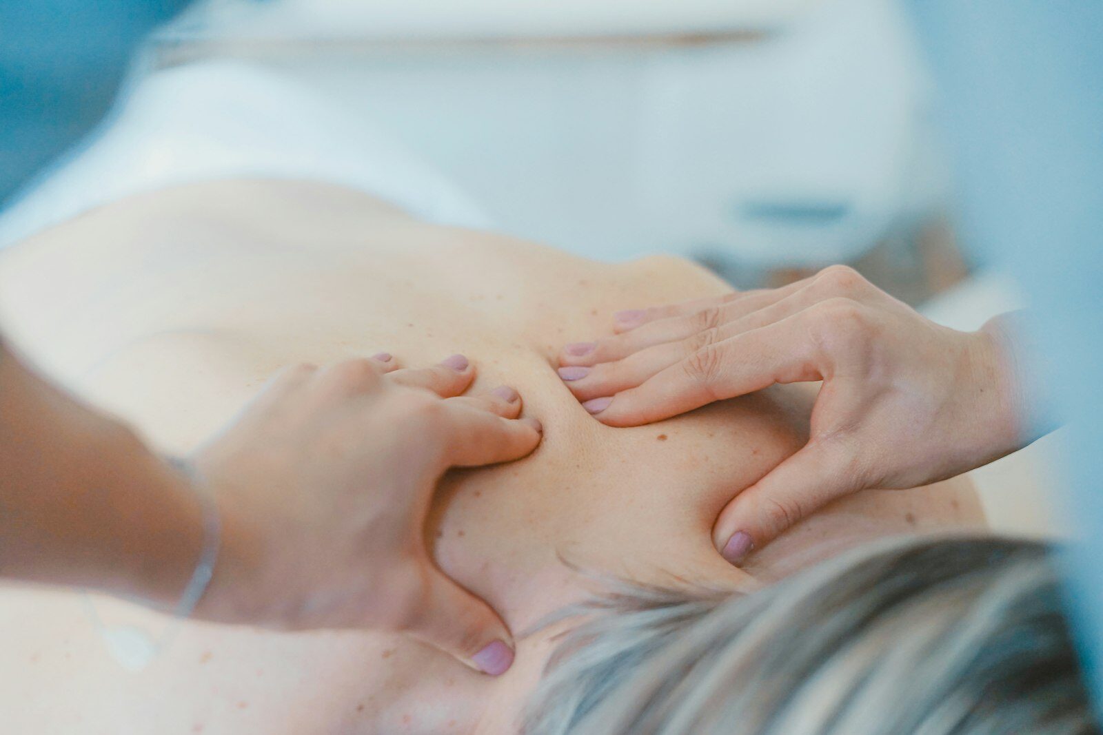 A practitioner's hands working on a patient's upper back.